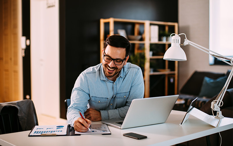 Man making notes while using a laptop